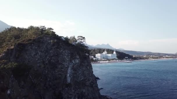 Vídeo. Vista aérea del hotel en la orilla del mar y las montañas cubiertas de bosque verde, árboles con cielo azul al amanecer. Vídeo. Vista aérea en la orilla del mar con hotel de lujo con fondo de bosque y montañas — Vídeos de Stock