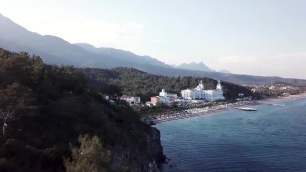 Video. Flygfoto över Hotel på havsstranden och berg täckta med gröna skog, träd med blå himmel vid soluppgången. Video. Flygfoto på havsstranden med lyx hotell med skog och berg bakgrund — Stockvideo