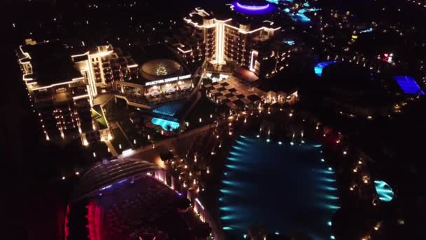 Aerial view on luxury resort hotel territory at night. Video. Night view of illuminated inner territory of hotel complex with footpaths, palms and pool. Tropical resort hotels at night top view. — Stock Video