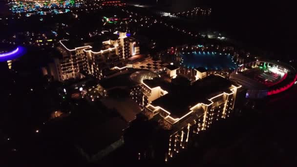 Vista aérea sobre el territorio del hotel resort de lujo por la noche. Vídeo. Vista nocturna del interior iluminado del complejo hotelero con senderos, palmeras y piscina. Hoteles tropicales en la noche vista superior . — Vídeo de stock