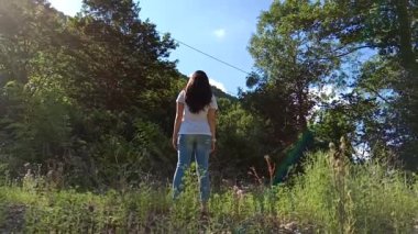 Kız tribünde bir orman. ağır çekim güzel bir genç kızın üzerinde güneşin görünüyor. Arkadan görünüm. Bir kamerada güzel bir gün. Bir buket çiçek ve ellerini kaldırdı ile duran genç kadın. Orman ve