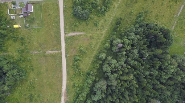 Aerial top view of country road through fields and forests in summer. Clip. Top view of the forest area with road.