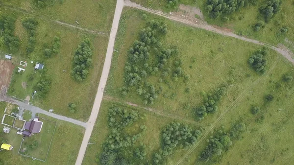 Vista aérea de la carretera de campo a través de campos y bosques en verano. Clip. Vista superior de la zona forestal con carretera — Foto de Stock