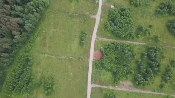 Vista aérea de la carretera de campo a través de campos y bosques en verano. Clip. Vista superior de la zona forestal con carretera — Vídeo de stock