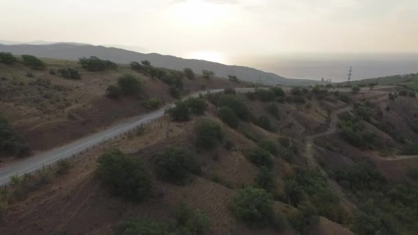 山の中の舗装道路の平面図です。ショット。道路、山、夕日で海の美しい景色 — ストック動画