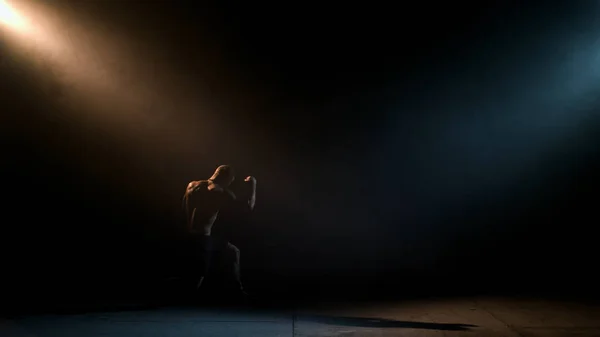 Boxeador haciendo sombra Boxeando en una habitación oscura. El hombre de la construcción atlética hace un golpe. Iluminación dramática — Foto de Stock