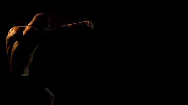 Boxeador haciendo sombra Boxeando en una habitación oscura. El hombre de la construcción atlética hace un golpe. Iluminación dramática —  Fotos de Stock