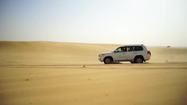 Flygfoto på Off-road äventyr med Suv i Arabiska öknen vid solnedgången med Dubais stadssilhuett eller stadsbilden. Öknen turnera med Suv. Offroad Suv ridning i öknen. Kör en 4-hjulsdrift Suv på den — Stockvideo