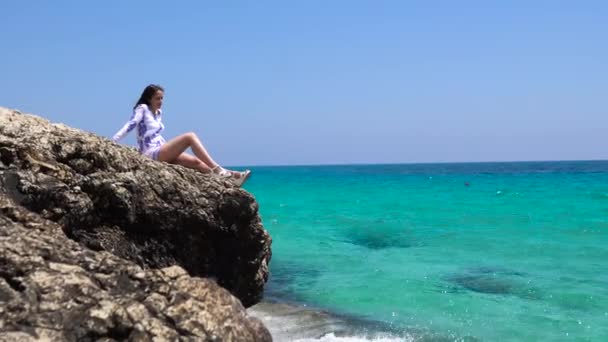 Mujer atractiva sentada en piedra cerca del agua. Hermosa mujer sentada en una roca cerca del mar — Vídeo de stock