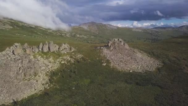 Luftaufnahme auf einer grünen Wiese mit einsamen Felsen und bewölktem Himmel. atemberaubende Berglandschaft mit großen Felsen mitten im Gras. Luftaufnahme der Bergseite — Stockvideo