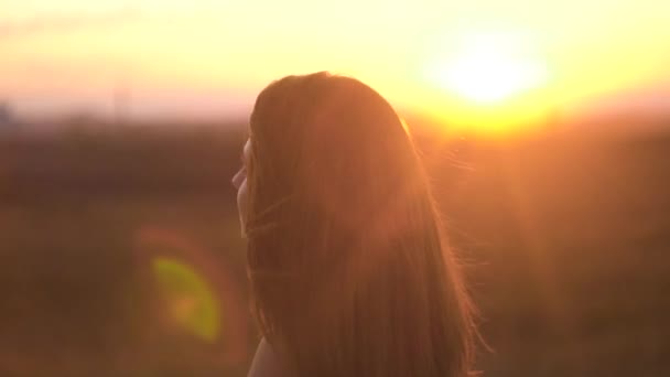 Retrato de una hermosa mujer de pelo largo sobre el fondo de los rayos del sol al atardecer. Mujer encantadora con el pelo revoloteando en el viento en los rayos de la puesta del sol — Vídeo de stock