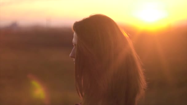 Retrato de una hermosa mujer de pelo largo sobre el fondo de los rayos del sol al atardecer. Mujer encantadora con el pelo revoloteando en el viento en los rayos de la puesta del sol — Vídeo de stock