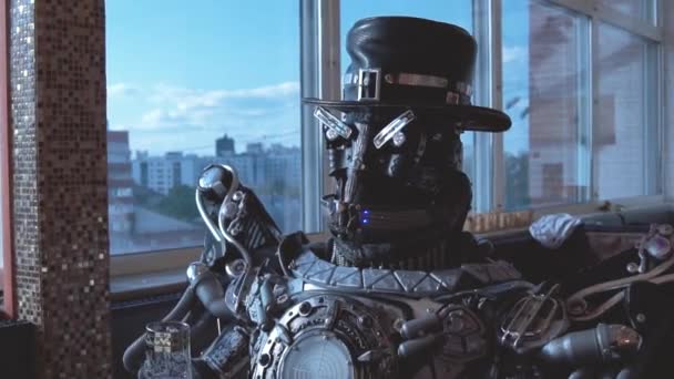 都市の高層ビルの眺めの背景にワインのグラスとレストランでテーブルに座って金属アンドロイド。映像。ロボット人間は、人間のような動作します。技術コンセプト — ストック動画