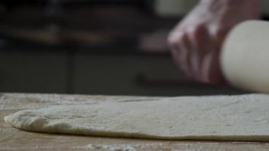 Mutfak masasının üstünde dışarı hamur haddeleme dostum, kapat. Sahne. Aşçı bir oklava ile mutfak masasının üzerinde bir parça hamur rulo. Görünümü kapatın. Pişirme kavramı ve ev yapımı yemek