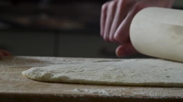 Um homem a distribuir massa na mesa da cozinha, de perto. Cena. O cozinheiro rola um pedaço de massa na mesa da cozinha com um rolo. Vista de perto. Conceito de cozinha e refeição caseira — Vídeo de Stock