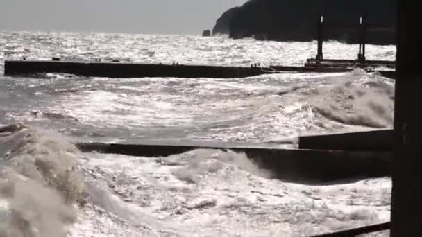 大きな波は、夕日を背景に防波堤クローズ アップについて中断されます。ショット。海の風景。海の水の嵐波石の桟橋、日当たりの良い、風の強い日を打ちます。太陽に照らされた海桟橋 — ストック動画