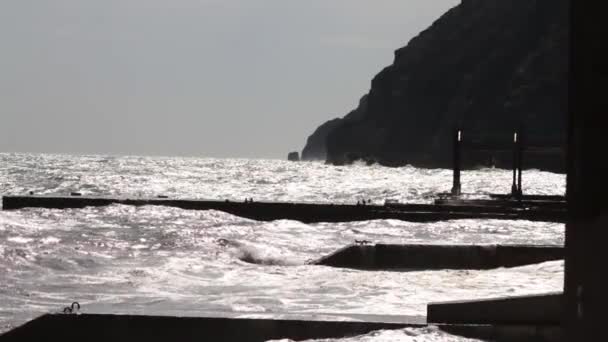 En stor våg bryter om en vågbrytare närbild mot solnedgången bakgrund. Skott. Marinmålning. Vatten storm havsvågor slår den Stenpiren, solig och blåsig dag. Havet piren upplyst av solen — Stockvideo