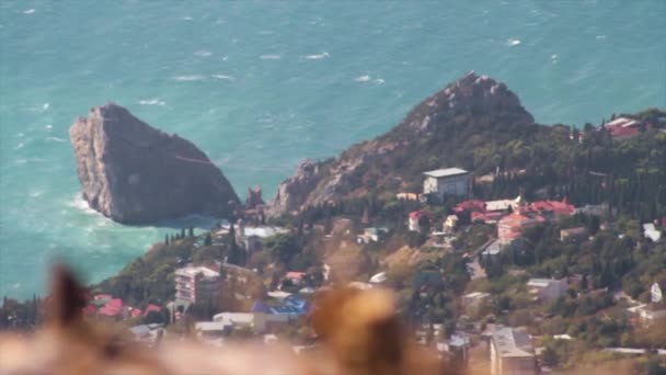 Vista panorámica de la orilla del mar con una enorme roca y un pequeño fondo de la ciudad. Le dispararon. Vista de la bahía de mar y la ciudad en la bahía desde las rocas, hermoso paisaje marino en un día soleado de verano, mar azul y cielo azul . — Vídeos de Stock