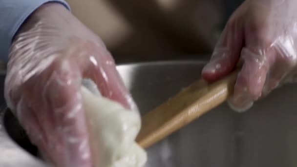 Allungamento della pasta. Scena. Stendere un impasto tra due mani in ciotola di metallo con acqua, fondo scuro. Impastare la pasta con le dita — Video Stock