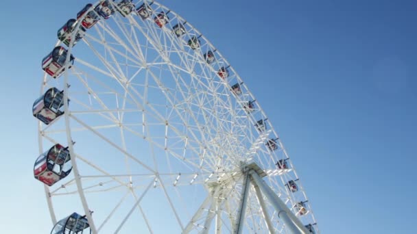 Fragmento de una atracción de noria con taxis cerrados de cerca sobre un fondo de cielo azul, vista inferior. Escena. Rueda de la fortuna en un día soleado contra un cielo azul claro. Disparo en el punto inferior. Abajo. — Vídeos de Stock