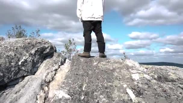 Young man standing on edge of cliff enjoying scenery. Footage. View of man from back on top of cliff. Person engaged in sports has conquered top and enjoys his success — Stock Video