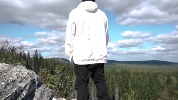 Joven parado al borde del acantilado disfrutando del paisaje. Filmación. Vista del hombre desde atrás en la cima del acantilado. Persona dedicada al deporte ha conquistado la cima y disfruta de su éxito — Vídeo de stock