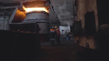 Karanlık kirli fabrika arka plan üzerinde üniforma ve kask arkadan iki işçi görünümünü. Görüntüleri. Üretim iki çalışanı monitör ve kontrol çalışmaları