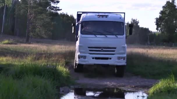 Moscow, Russia - September, 2018: Freight vehicles traveling on country road with puddles. Scene. Truck rides on dusty road and passes puddle in forest. Transportation of rural goods — Stock Video