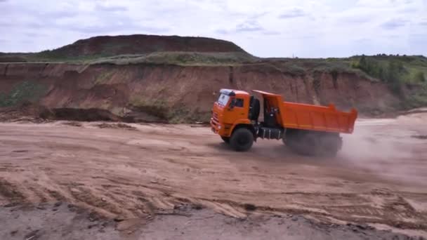 Vista del camión volquete de conducción en suelo arenoso. Escena. Camión volquete naranja cabalga en cantera con tierra en tierras bajas — Vídeo de stock