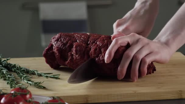 Primer plano del trozo de jamón. Escena. Cortado por las manos de las mujeres en dos partes trozo de jamón jugoso. Jamón en rodajas sobre tabla de madera sobre fondo de ramitas verdes de verduras y tomates — Vídeo de stock