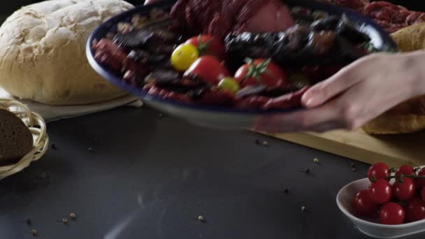 Разрезание мяса на тарелке помидорами. Сцена. Закрыть тарелку с изысканной нарезанной ветчиной и мясом с помидорами. Мясо кулинарное блюдо на фоне свежих трав и хлеба — стоковое видео