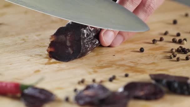Closeup nůž řeže klobása. Scénu. Detail řezání tmavě salám na dřevěném prkénku. Sůl na pozadí krásných koření — Stock video