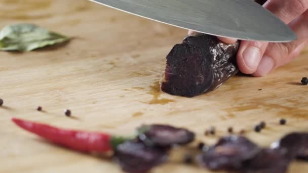 Close-up van mes snijdt de worst. Scène. Close-up van het snijden van donkere salami op houten snijplank. Zout op de achtergrond van prachtige kruiden — Stockvideo