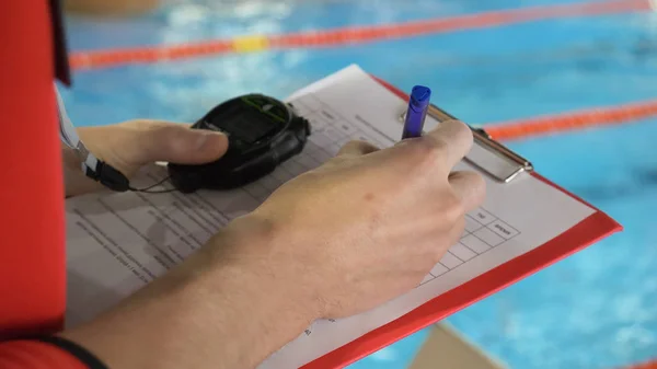 Juez en la competencia en la piscina. Primer plano de la mano de los jueces en la piscina que registra el testimonio en la hoja —  Fotos de Stock