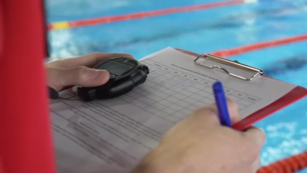 Rechter in competitie in zwembad. Close-up van de hand van de rechters in het zwembad die de getuigenis in het blad registreert — Stockvideo