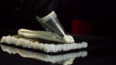 Hazırlama süreci yakından görmek rulo suşi. Şef eldiven pilav ile nori yaprağının üzerinde dolgu Krem pasta çantasından getirir. Suşi rulo yapma sanatı