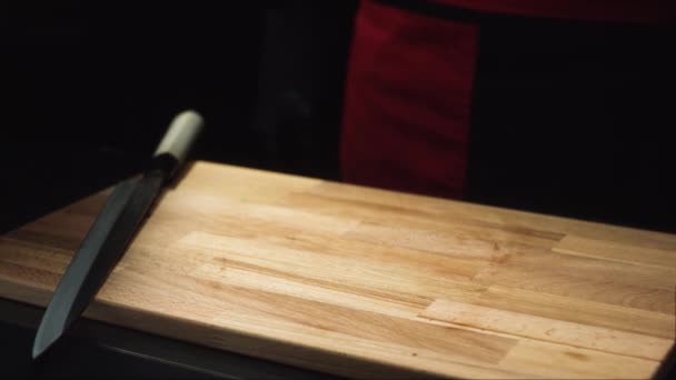 Close-up of knife on cutting board. Wooden board and knife ready to cook on dark background. Items for cutting and cooking — Stock Video