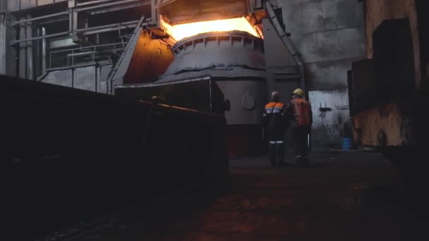 Vista de dos trabajadores de la espalda en uniforme y cascos en el fondo de la fábrica sucia oscura. Filmación. Dos empleados supervisan y controlan el trabajo de producción — Vídeos de Stock