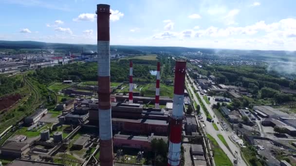 Paisaje urbano con planta de construcción industrial con tres tuberías industriales altas rojas y blancas sobre un cielo azul claro sin nubes en un día soleado. Filmación. Vista superior cerca de las chimeneas blanco-rojas de la planta. Concepto de — Vídeo de stock