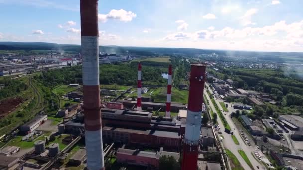 Paisaje urbano con planta de construcción industrial con tres tuberías industriales altas rojas y blancas sobre un cielo azul claro sin nubes en un día soleado. Filmación. Vista superior cerca de las chimeneas blanco-rojas de la planta. Concepto de — Vídeo de stock