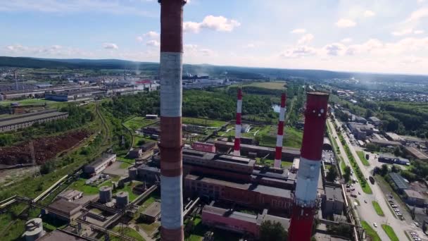 Paisaje urbano con planta de construcción industrial con tres tuberías industriales altas rojas y blancas sobre un cielo azul claro sin nubes en un día soleado. Filmación. Vista superior cerca de las chimeneas blanco-rojas de la planta. Concepto de — Vídeo de stock