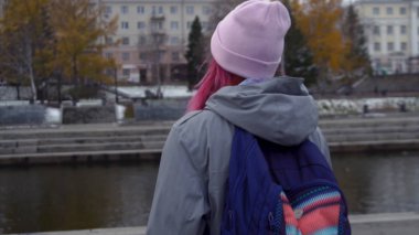 Arka görünüm sırt çantası şapkalı kadınla hipster close-up. Pembe saçlı ve sonbahar cityscape arka plan üzerinde pembe şapka genç güzel kadın