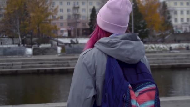 后视特写镜头的嬉皮士妇女与背包在帽子。年轻美丽的妇女与粉红色的头发和粉红色的帽子在秋天城市风景背景 — 图库视频影像