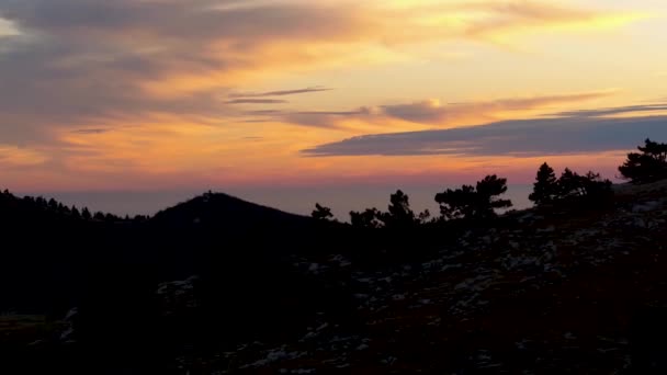 Schwarze Silhouette eines Hügels bei Sonnenuntergang mit Wolken. Schuss. Blick von oben auf malerischen Sonnenuntergang. Der Himmel ist in hellen Farben auf hügeligem Gelände gemalt — Stockvideo