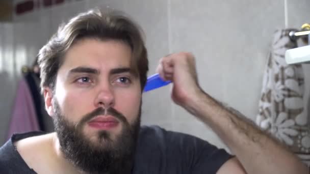 Man in the bathroom looking in a mirror and fixing his hair. Portrait of handsome man brushing his hair in bathroom. Reflection in the mirror of handsome man styling hair — Stock Video