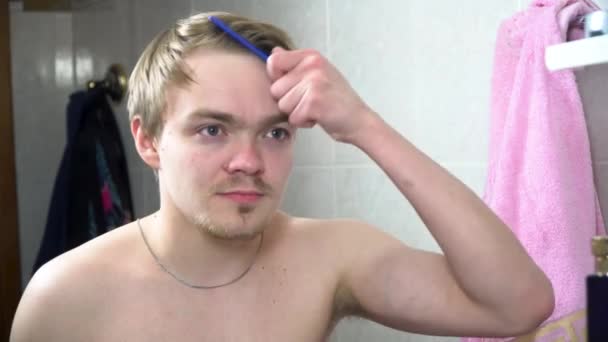 Man in de badkamer in een spiegel kijken en vaststelling van zijn haren. Portret van knappe man borstelen zijn haren in de badkamer. Reflectie in de spiegel van de knappe man styling haar — Stockvideo