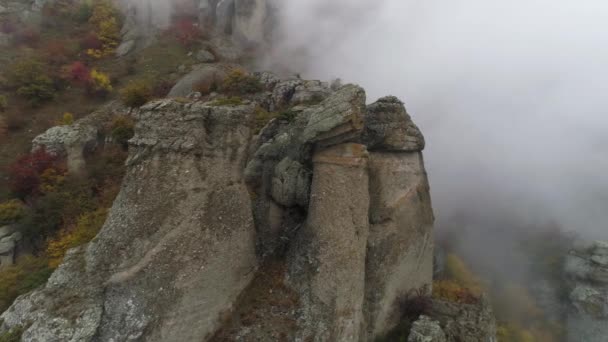 View near stone pillar of cliff. Shot. Top view of stone pillar of rock with approaching thick fog. Autumn landscape with colorful shrubs and dense gray fog on mountain — Stock Video