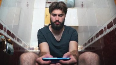 Tuvalette otururken bir akıllı telefon kullanan adam. Bir ileti yazmakta olduğunu.