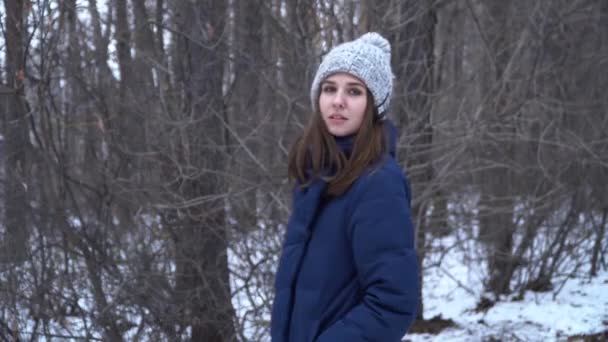 美丽的女孩在蓝色针织围巾户外在冬天的森林。漂亮的女孩看着相机 — 图库视频影像