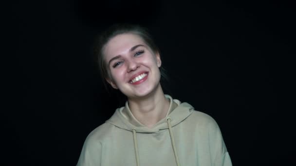 Retrato de cerca de una joven riéndose sobre un fondo negro. Es muy positiva. . — Vídeos de Stock